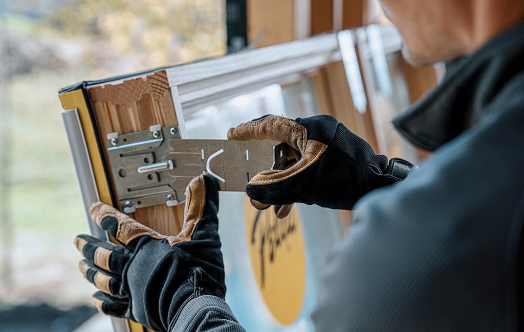 A man wearing gloves is manipulating a silver clip on a new window frame .