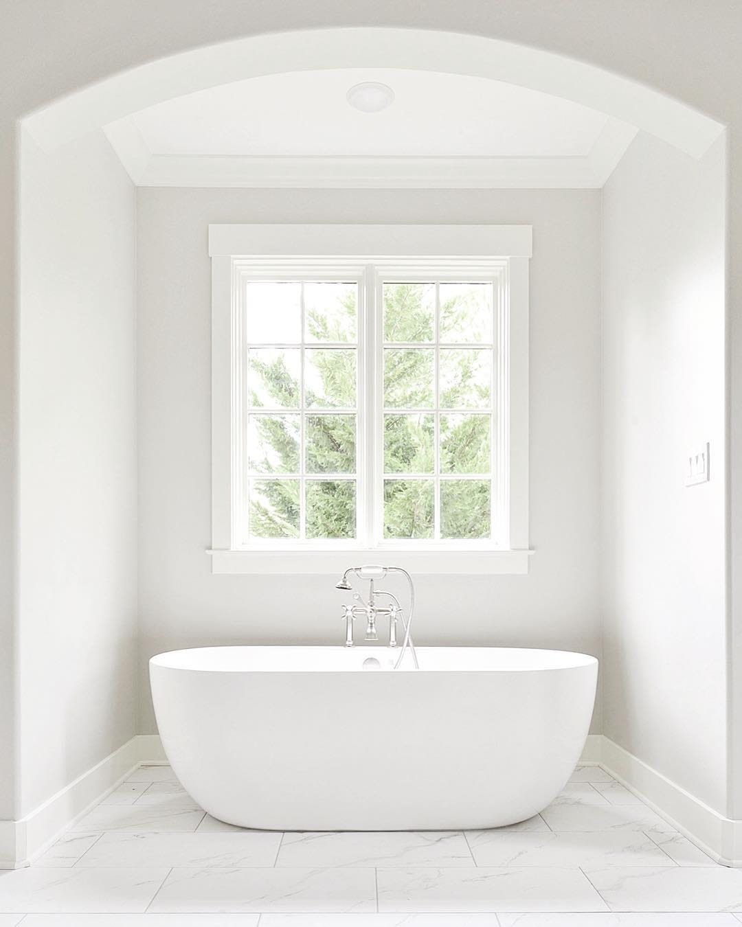 Casement Window Brings Touch Of Elegance To White Bathroom White on white bathroom with large casement window over freestanding tub