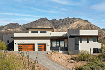 A contemporary home in the southwestern mountains with two orangish garage doors and high altitude glass for energy efficiency.