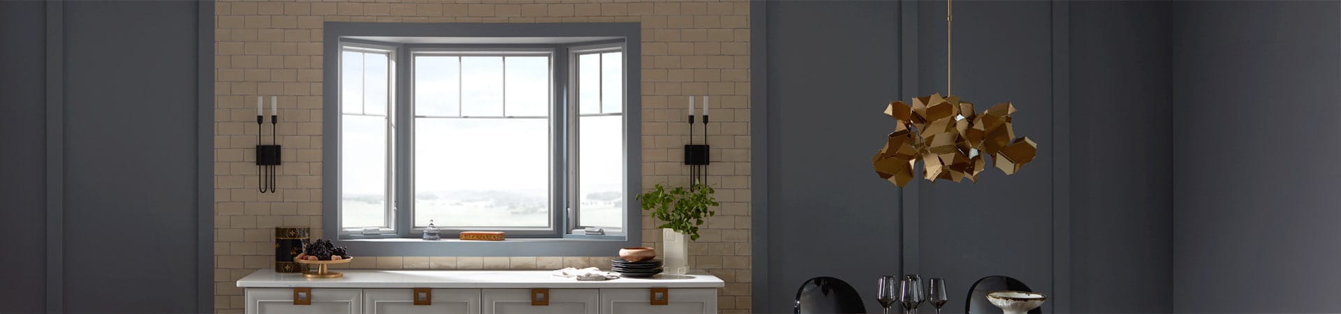 A modern kitchen featuring a bow window, gray walls, and decorative lighting, with a stylish countertop setup.