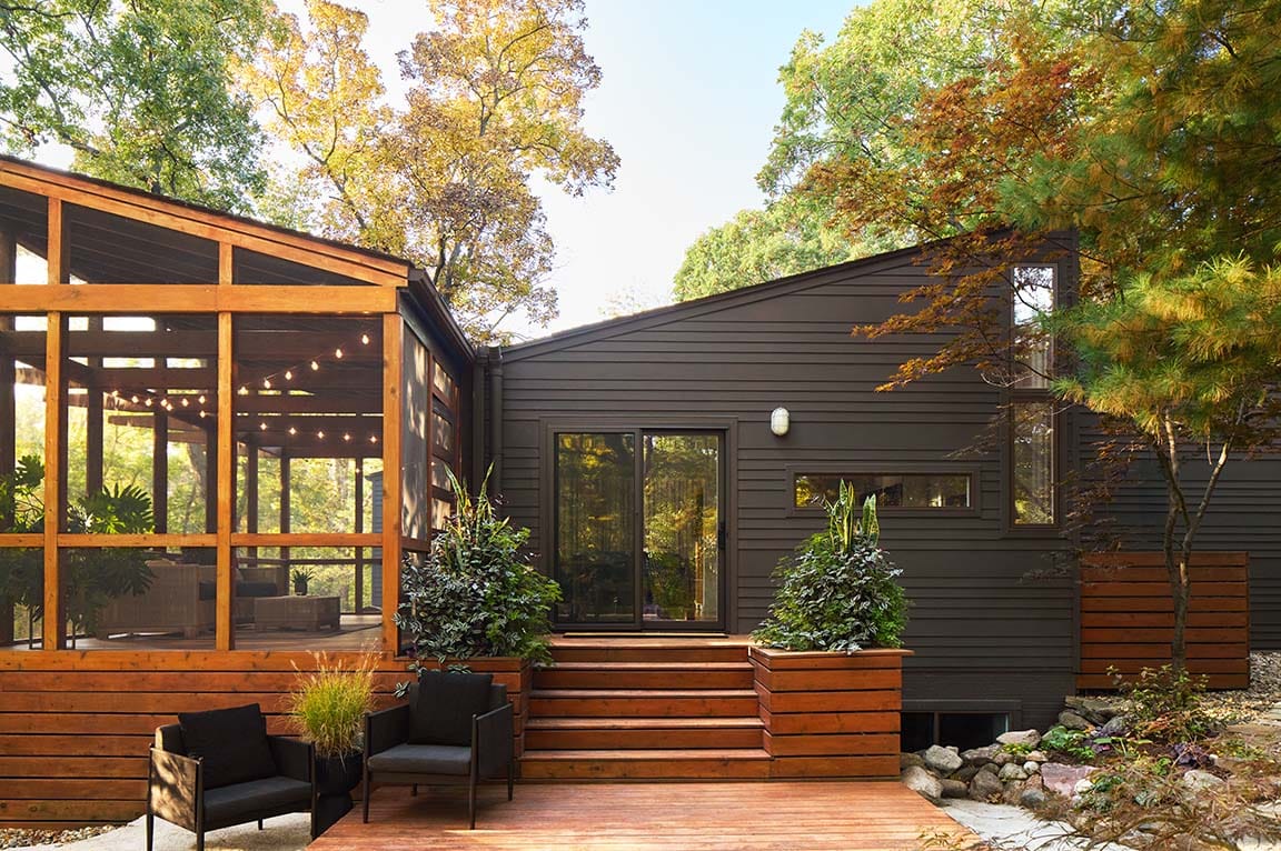 A natural-framed cabin that includes a large sunroom opens using a black sliding patio door.