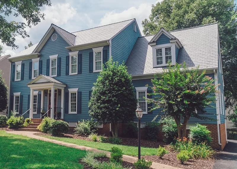 The exterior of a colonial-style home features blue siding with white vinyl windows.