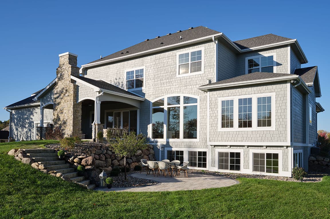 The exterior of a large home that's facing the sun, which is shining into all windows, including several basement sliding windows.