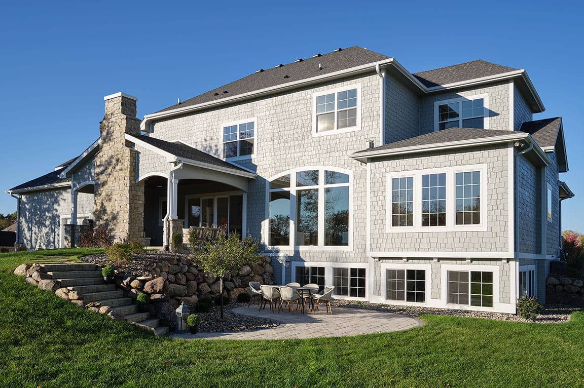 The exterior of a large home that's facing the sun, which is shining into all windows, including several basement sliding windows.