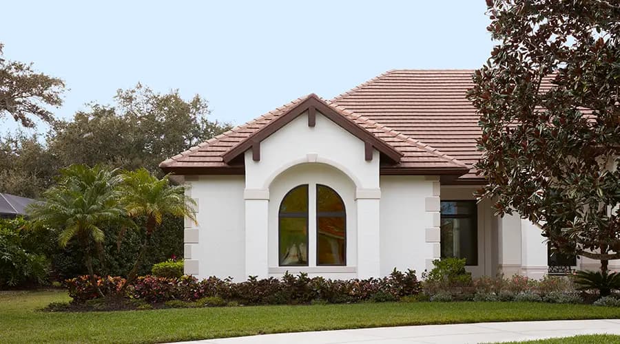 White stucco Mediterranean-style single-story house exterior with arched window, red clay tile roof and landscaped front yard with palm trees
