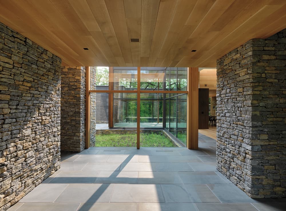 Natural Wood Windows Used In Modern Design Hallway with stone walls on either side, wood plank ceiling, and wall of picture windows ahead