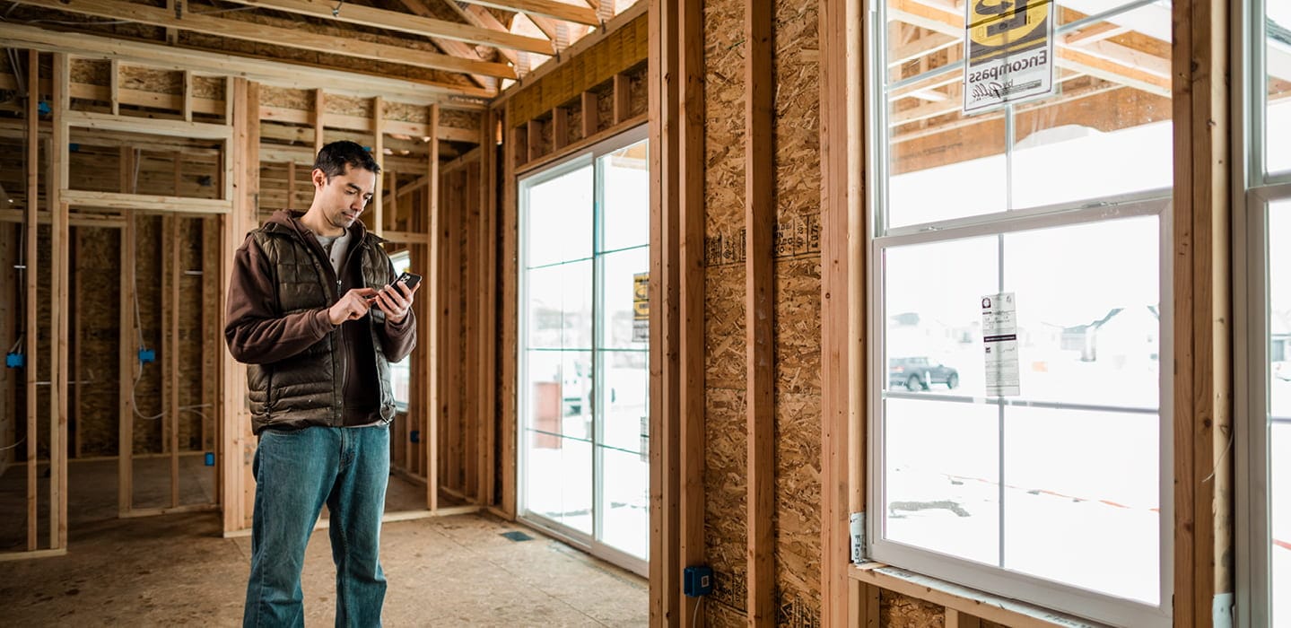 construction working standing in a room under construction looking at his phone