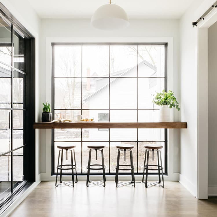A modern kitchen with a wooden bar and four stools, featuring a large floor-to-ceiling window.