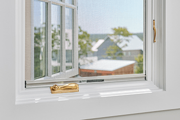 An open white casement window featuring a fold-away handle in brushed gold.