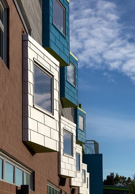 The side view of an apartment building, featuring custom jut-out panels with large fixed windows.