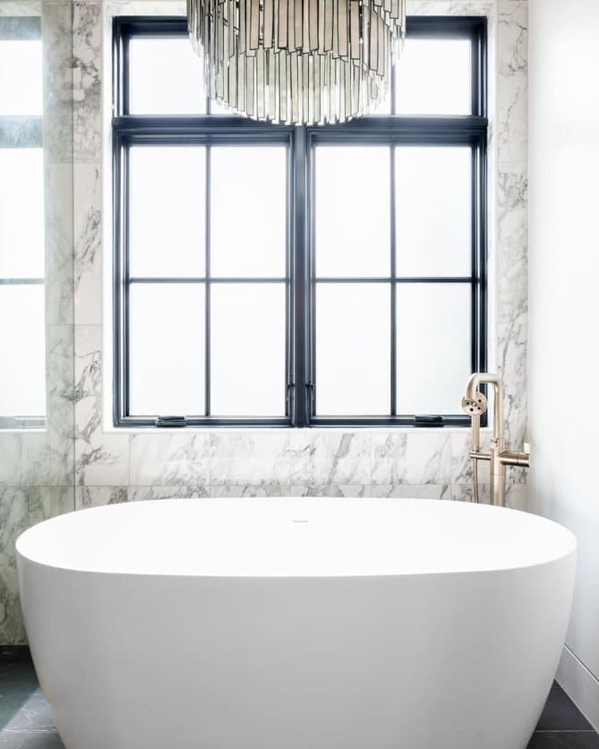 Black casement windows sit behind the bathtub in a modern bathroom.