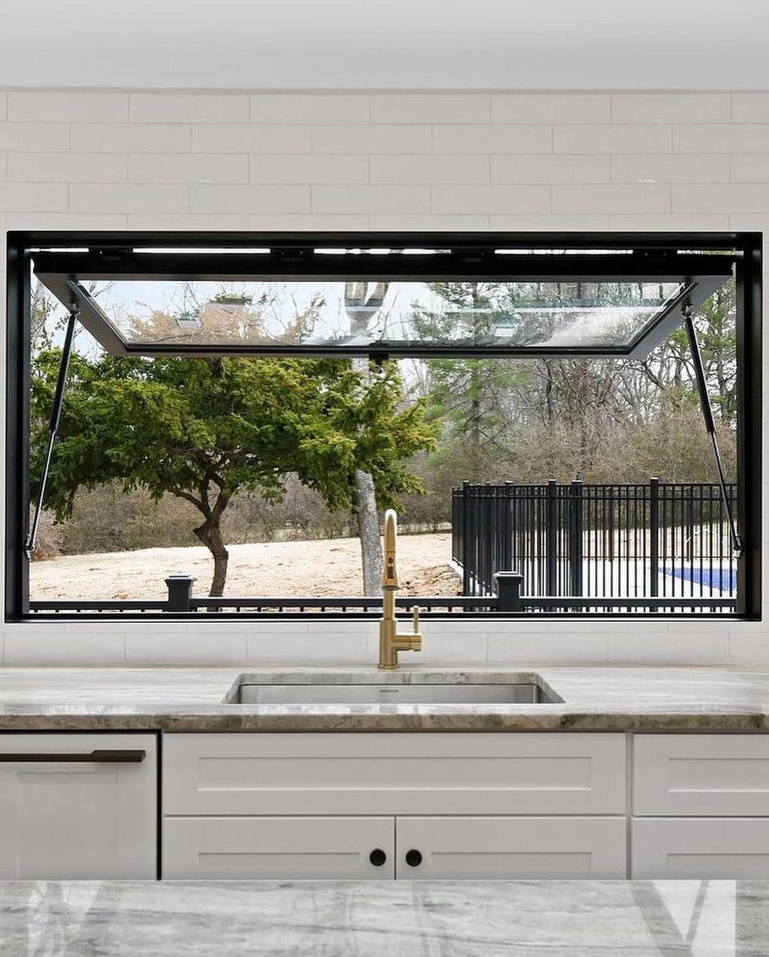 A black strut awning window sits behind the kitchen sink, overlooking the backyard.