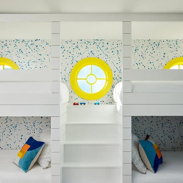 White bunk beds with round yellow windows featuring grilles in a playful kids' room.