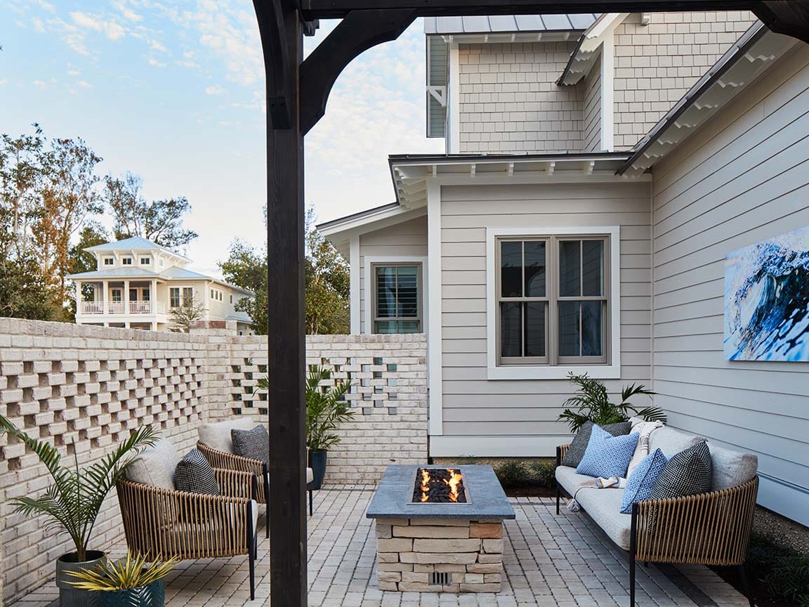 Modern outdoor patio with built‑in fire pit, cushioned seating, and light gray siding on a contemporary home.
