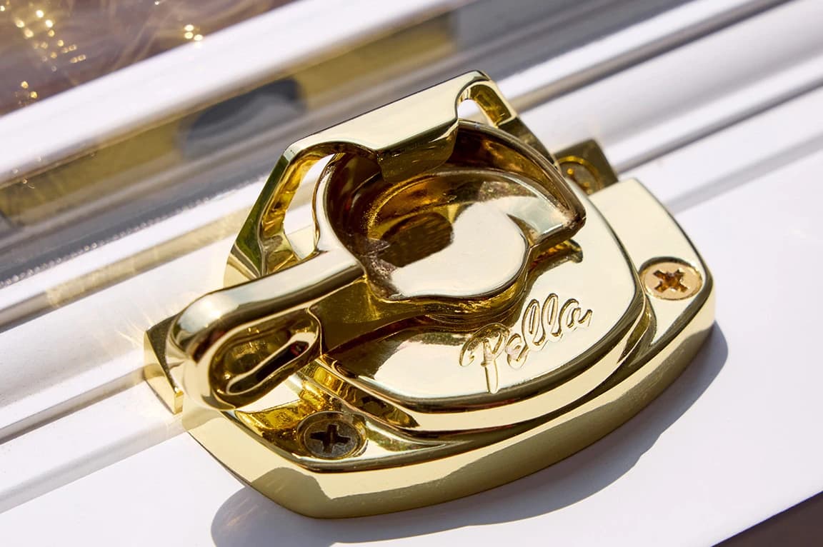 Gold window lock mechanism on a white frame, highlighting parts of a window.
