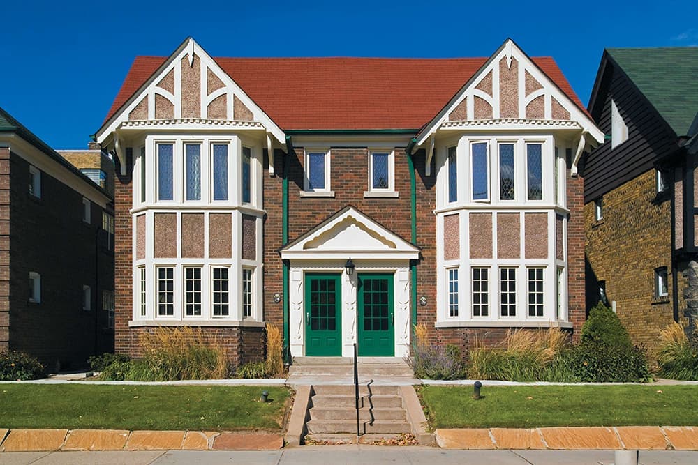 A large brick duplex with a green entry door on each side and white bow window units.