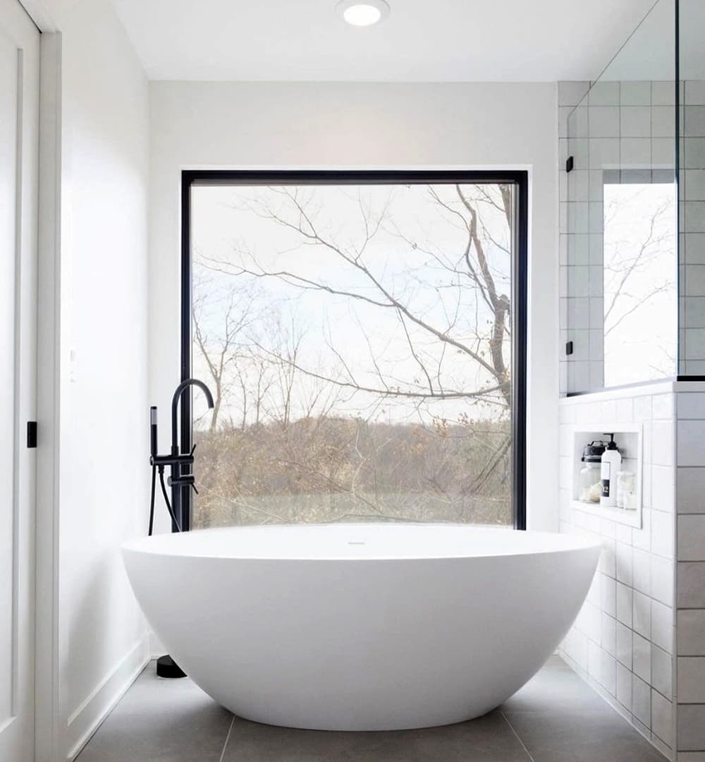 White bathroom features black rectangular window without grilles to light bathtub area.