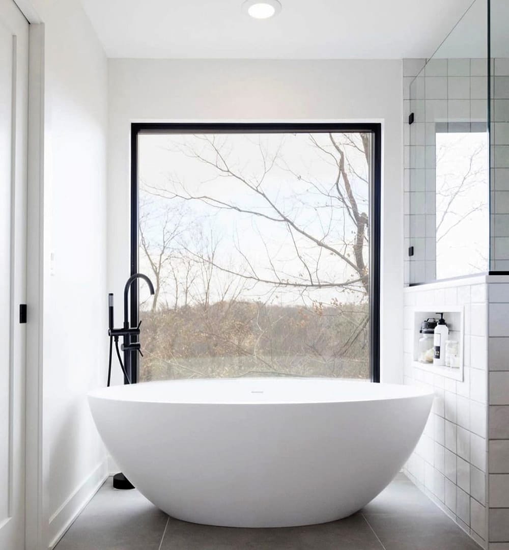 White bathroom features black rectangular window without grilles to light bathtub area.