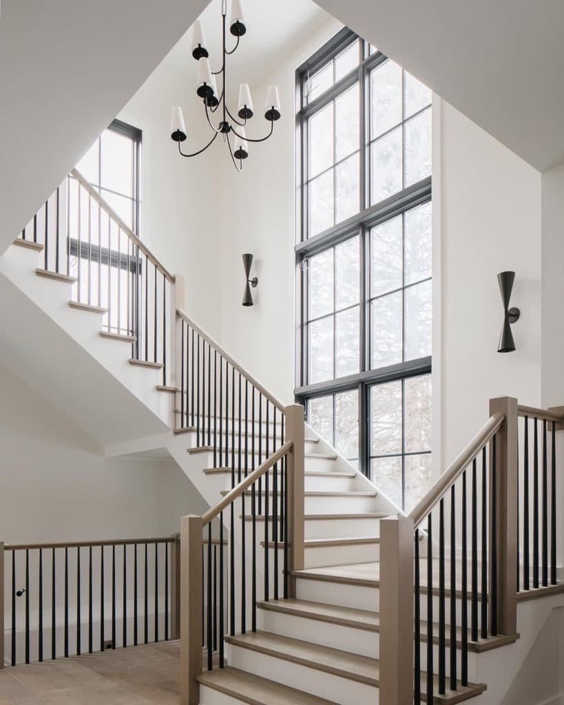 A tall staircase features wood and black banisters, complemented by massive black windows that span the entire ascent.