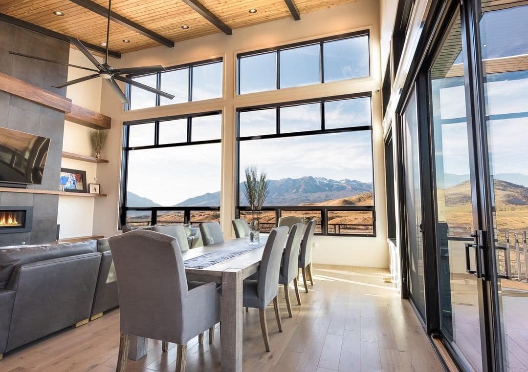 A contemporary dining and living room space features a large wall of black floor-to-ceiling windows.