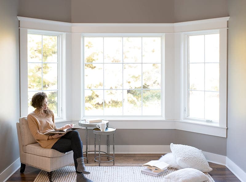 A young woman is reading peacefully in front of a bow window, which feature sound-resistant windows