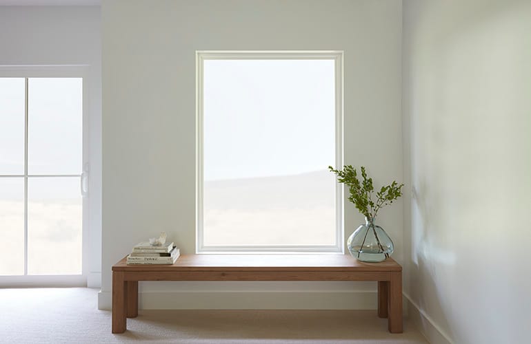 A long hall table with books and a plant on the top sits below a large vinyl picture window.