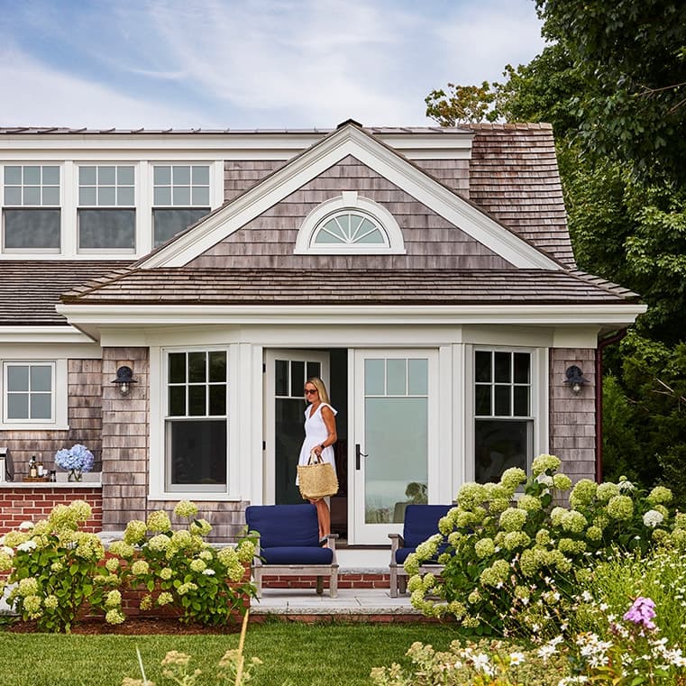 Woman walking outside of cottage style home in Cape Cod with hydrangeas.