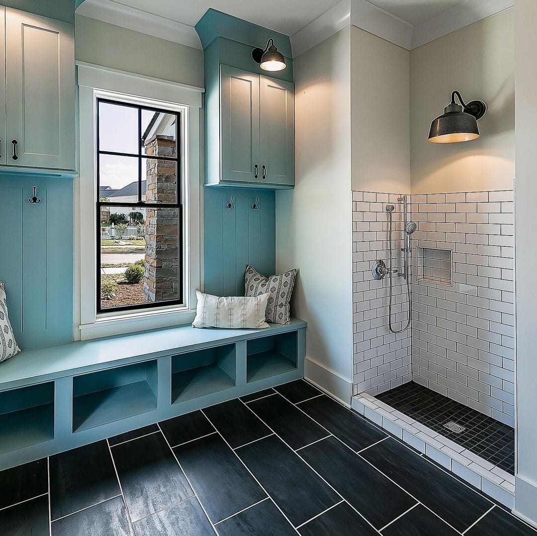 A black mudroom window is placed between light blue cabinets and above a window bench.