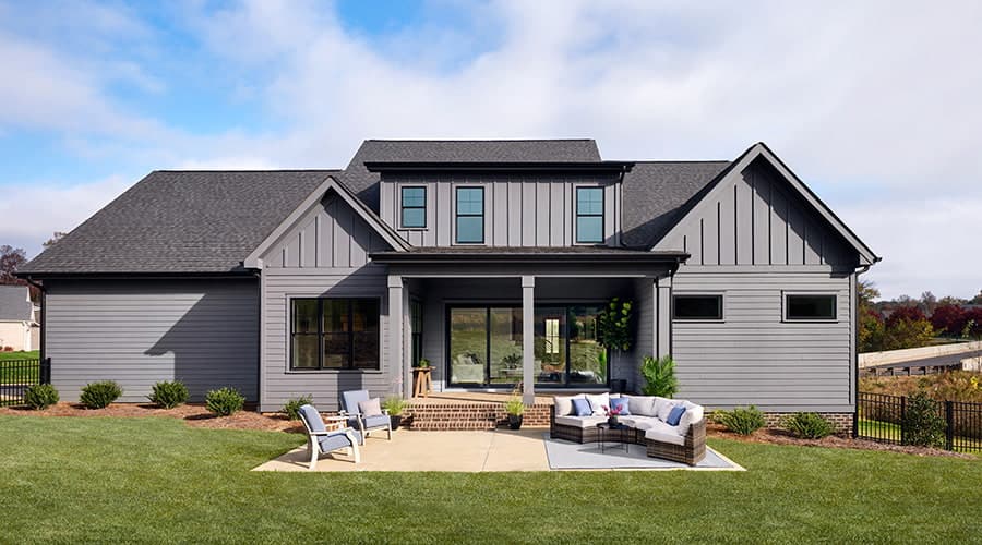 The backyard view of a home with gray siding and a large cement patio with comfortable outdoor furniture.