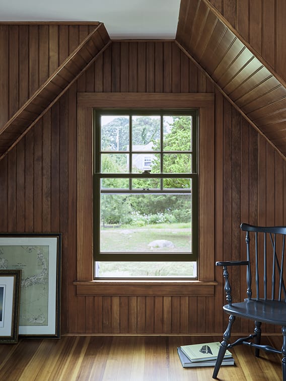 A cozy room featuring dark wood paneling and a classic interior window trim, with a view of greenery outside.