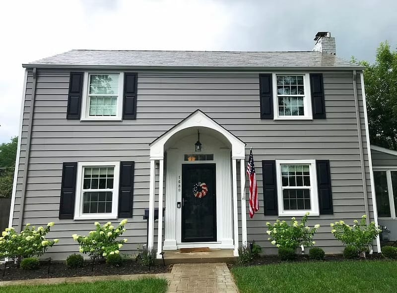 A gray traditional home has white single-hung windows with black shakers.