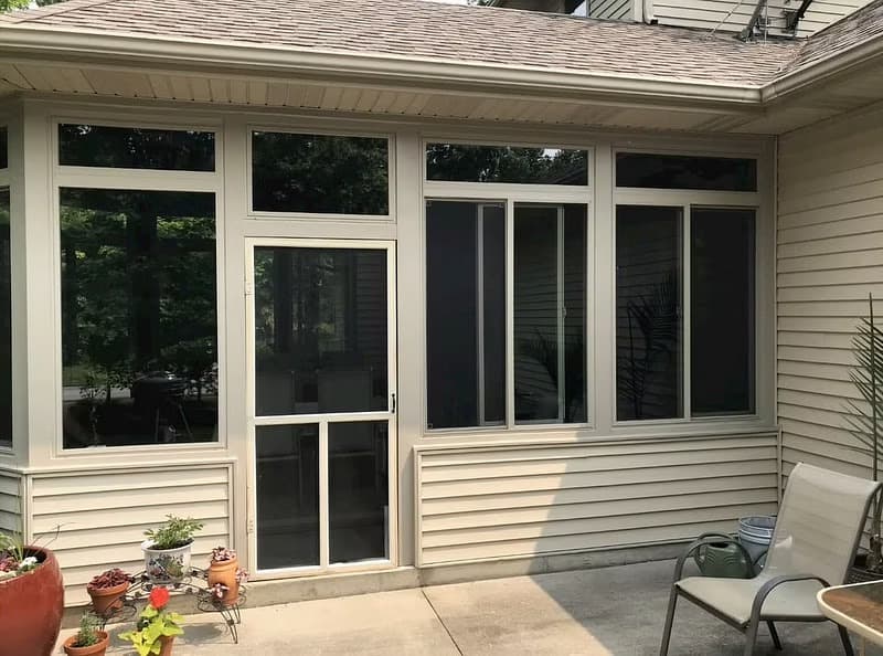 The exterior of a backyard sunroom with tan windows overlooking a garden.
