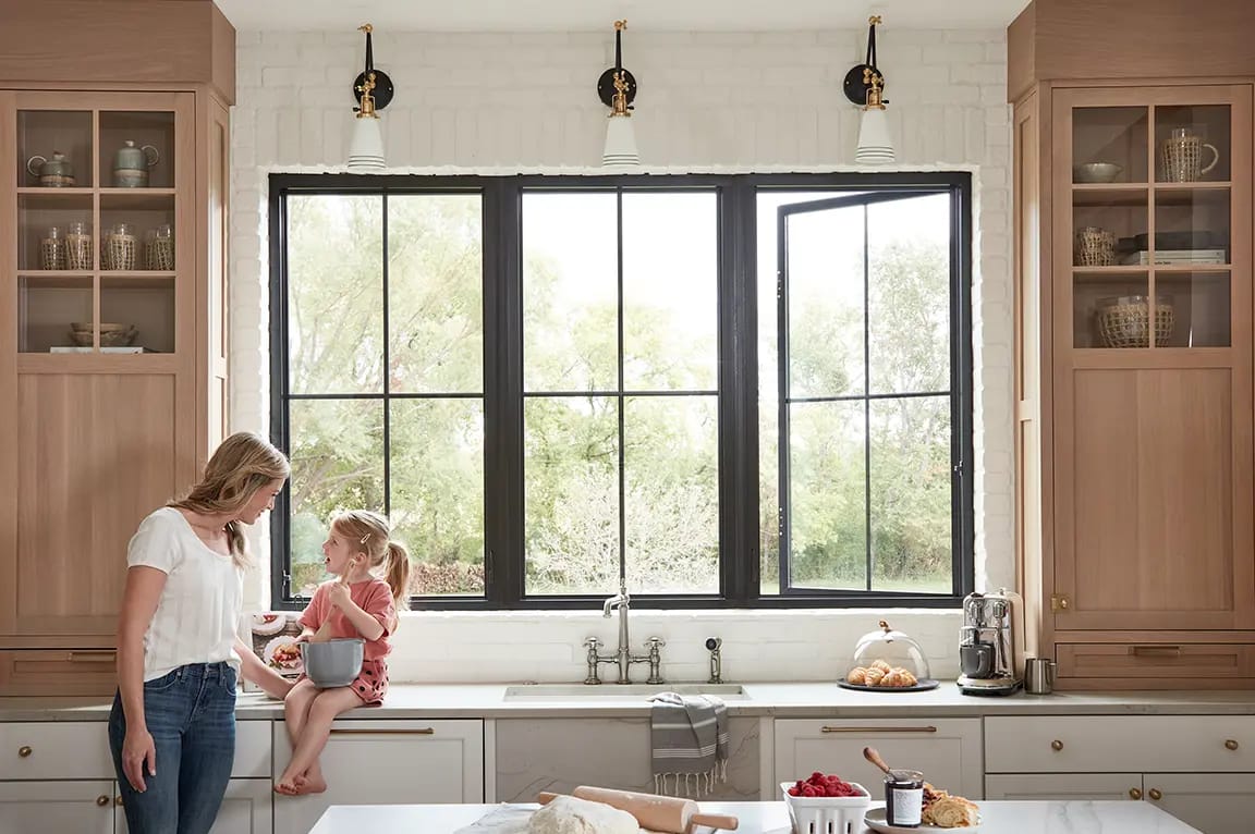 Bright farmhouse kitchen with black-framed windows, marble island showing dough and rolling pin, bowl of strawberries and pastries.