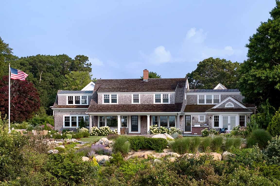 Cape Cod–style home exterior with large windows, landscaped yard, and traditional coastal design.