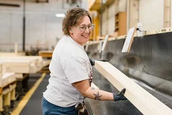 Smiling worker handling wood planks in a factory setting, showcasing careers in manufacturing.