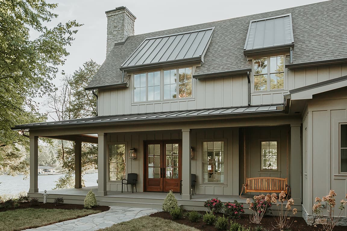 A modern house with gray windows and a welcoming porch, surrounded by greenery.