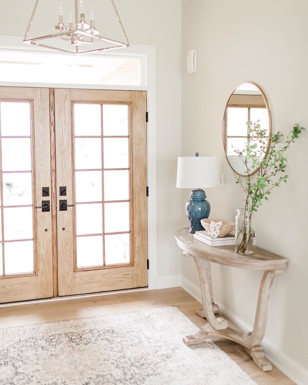 Wood French Patio Doors Light Farmhouse Style Entryway entryway with oak french patio doors and console table with blue lamp, round mirror, and greenery