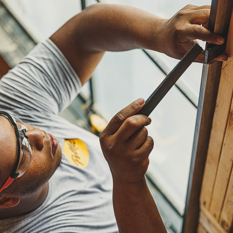 A man measuring a wooden frame for bow windows, showcasing craftsmanship and attention to detail.