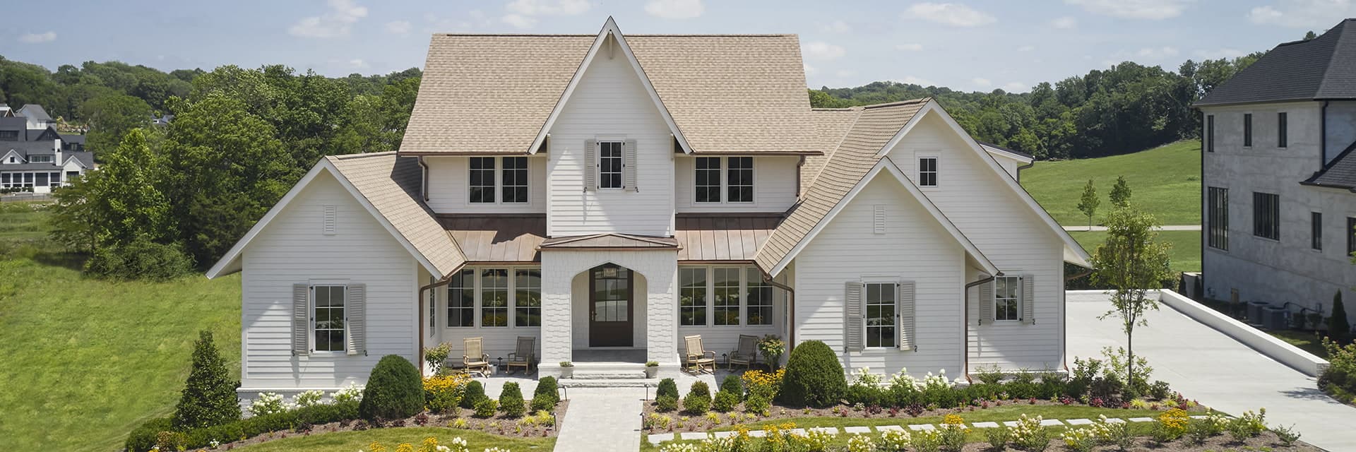 a two-story white home with many a-frame sections with well-tailored landscaping.