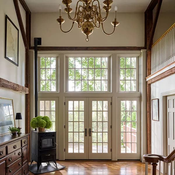 A grand entryway features combinations of French doors, mullioned windows, a brass chandelier, and exposed wood beams.