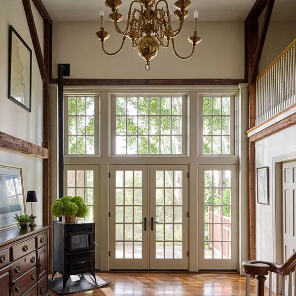 A grand entryway features combinations of French doors, mullioned windows, a brass chandelier, and exposed wood beams.