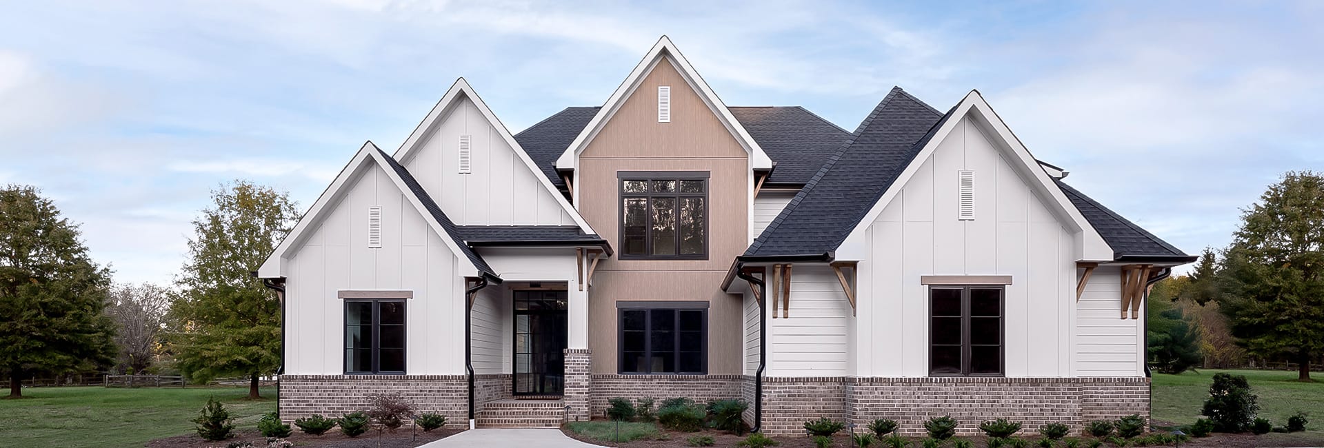 Modern two-story farmhouse exterior with white board-and-batten siding, black gabled roof, brick foundation and landscaped front yard