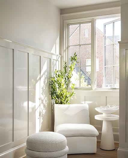 a mono-chromatic sitting area featuring a chair, footstool, plant and two casement windows open to let in the fresh air.
