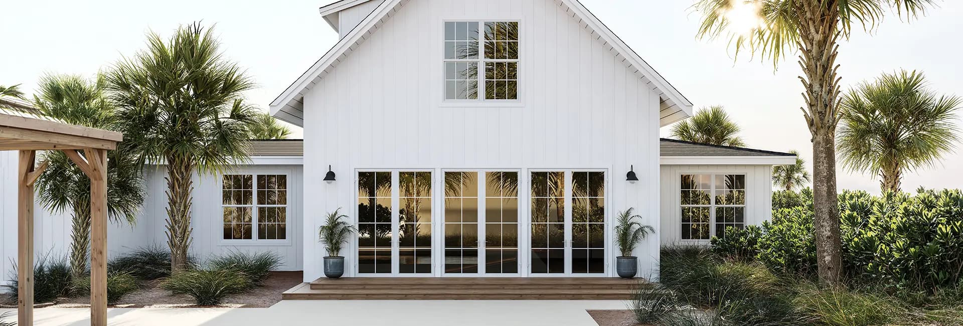 White beach house exterior with large glass French doors, wooden steps, potted palms and palm-tree landscaping