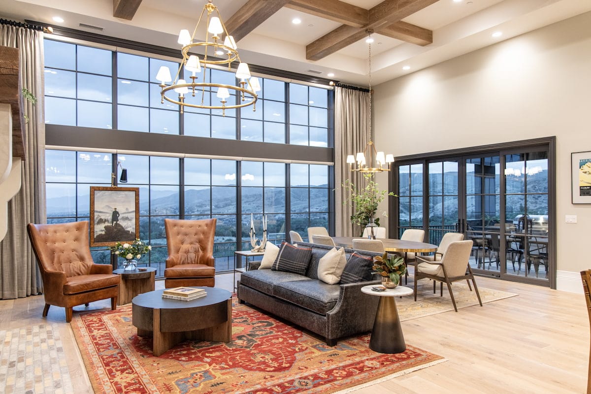A living room with a couch, chairs and dining table features a wall of gray windows with traditional grilles.