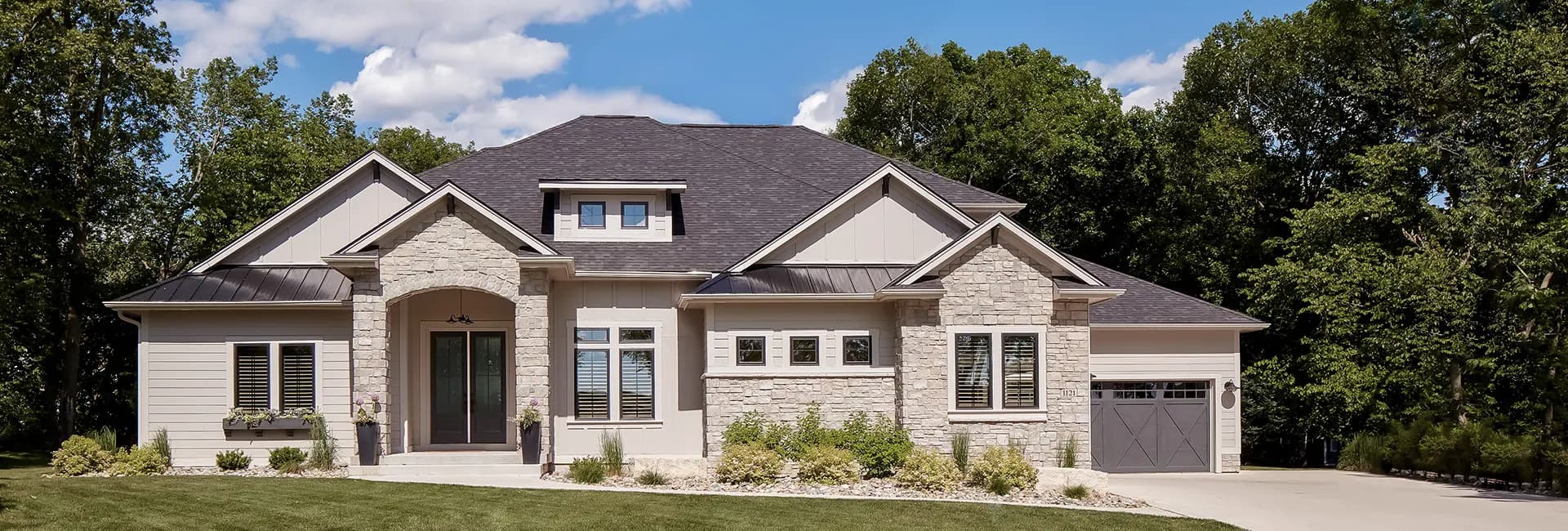 Modern suburban single-family home with stone facade, dark shingle roof, attached garage and landscaped front yard