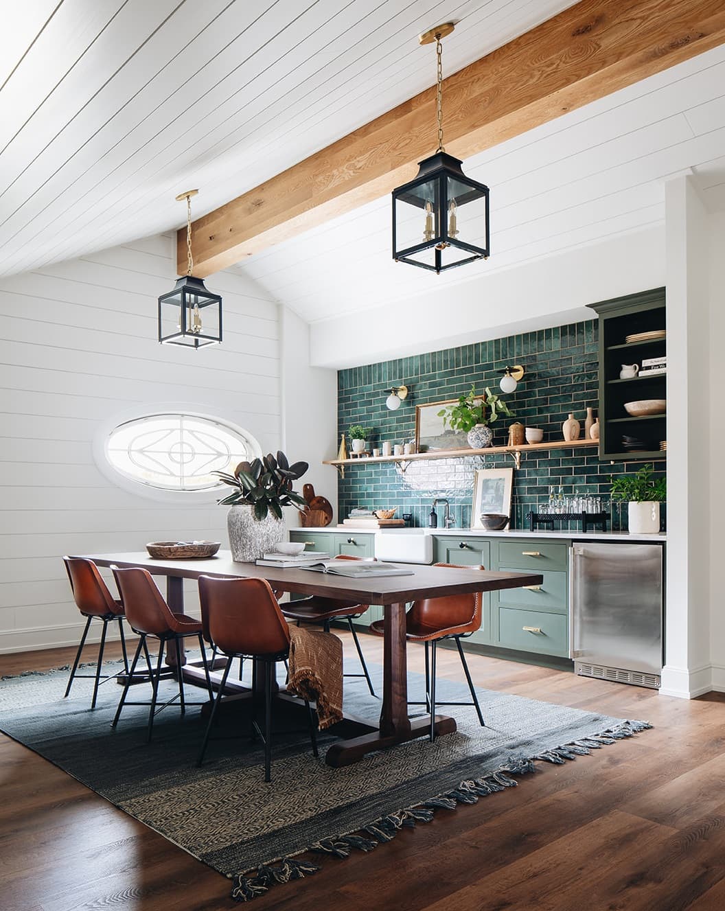 A white oval window with custom grilles lies on the back wall of a kitchen and dining area.