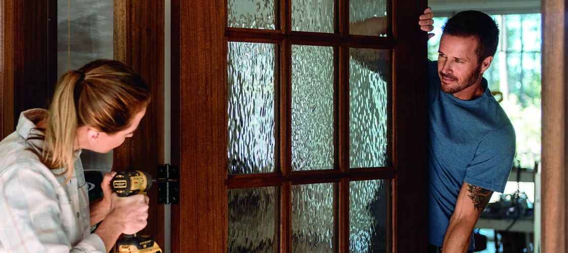 a man and woman working together to install a new wood front entry door