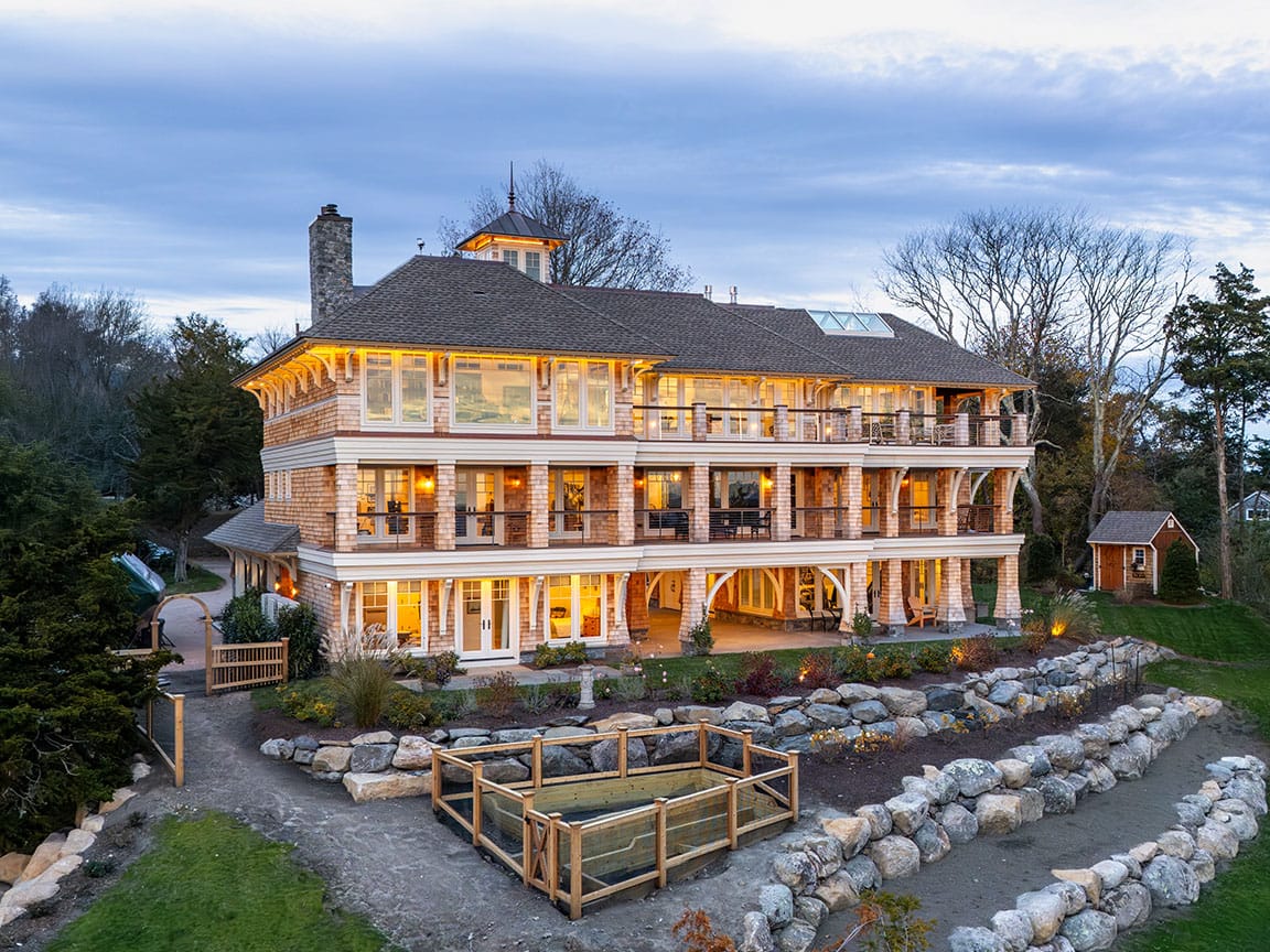 Large coastal home exterior with wraparound porch at dusk.