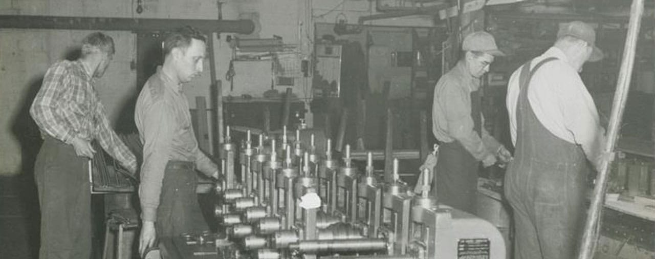 an old black-and-white photo of four men working in a manufacturing plant.